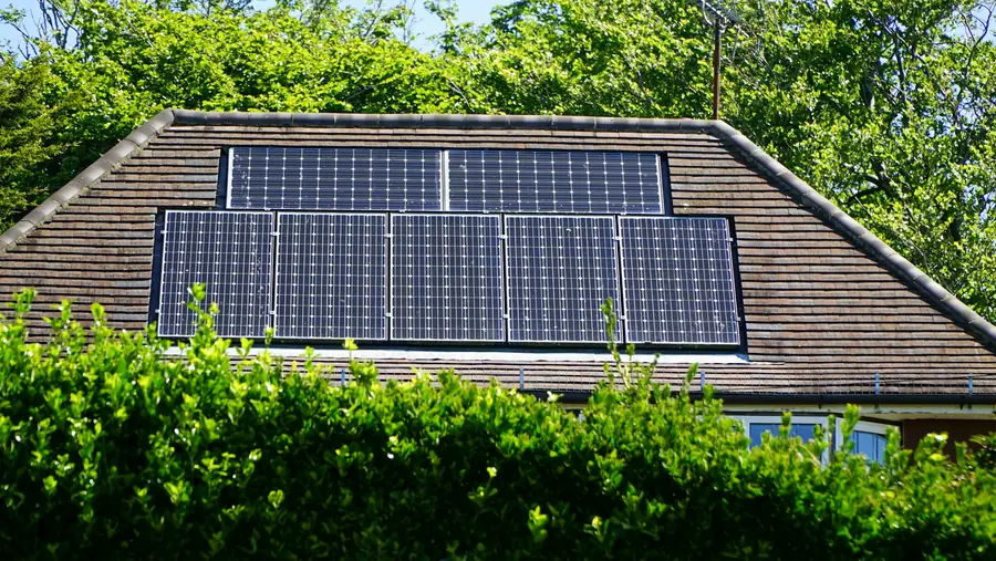 Solar panels on a house roof behind a garden hedge